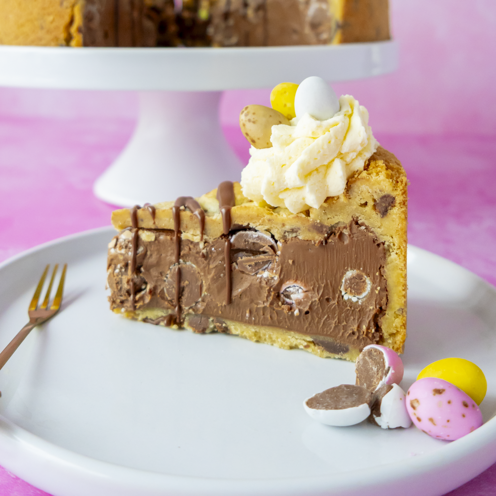 Slice of DoughGirl Easter cookie cake with chocolate drizzle on a white plate against a pink background