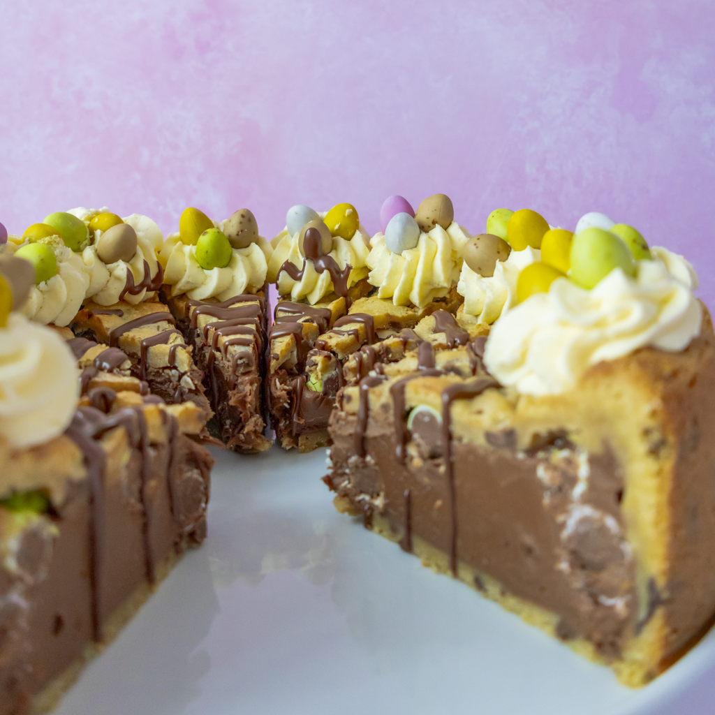 A pre-sliced Chocolate cookie pie with Easter-themed decorations on a white plate against a pink background