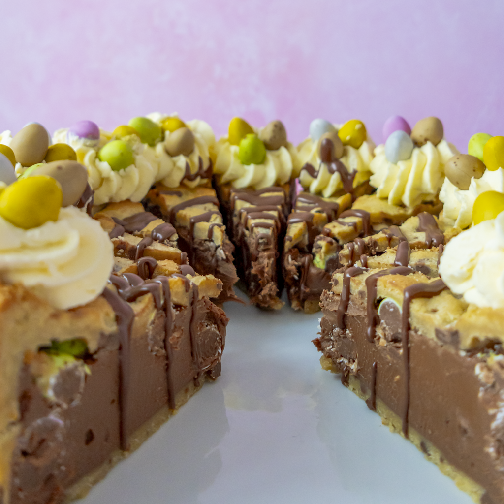 Close-up of a chocolate cookie pie topped with cream and MIni Eggs on a white plate against a pink background