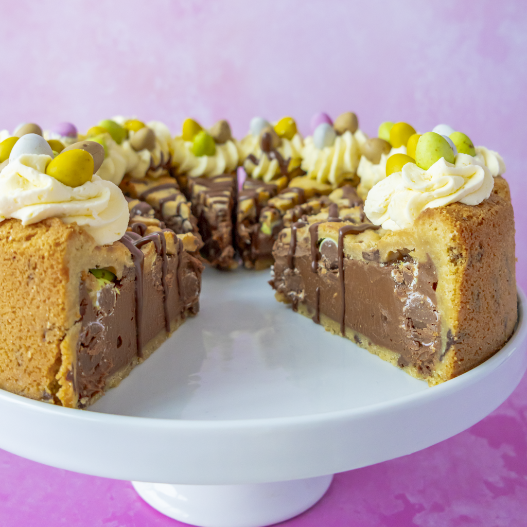 Multilayered pre-sliced cake with a slice removed on a white cake stand against a pink background