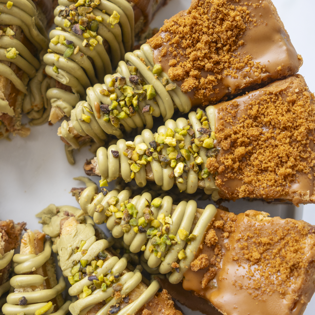 Close-up of several chocolate-dipped cookie pie pieces on a white surface, with green pistachio drizzle and crushed pistachio topping.