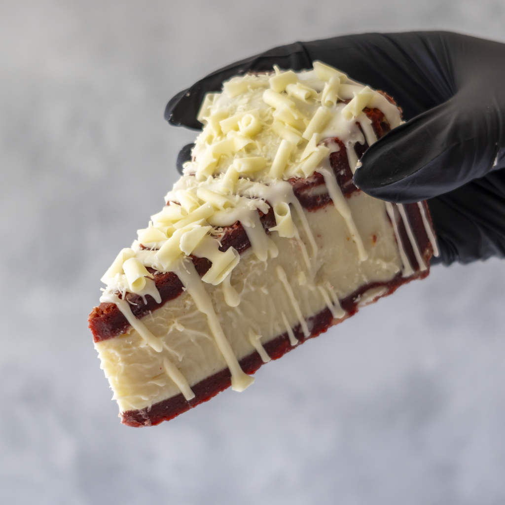 Red Velvet Cookie Pie Slice held in black glove showing creamy white chocolate layer