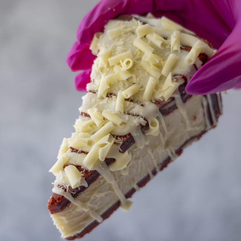 Red Velvet Cookie Pie Slice held in pink glove showing white chocolate topping