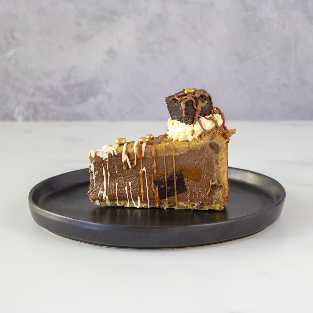 Slice of layered dessert with caramel drizzle on a black plate against a gray background