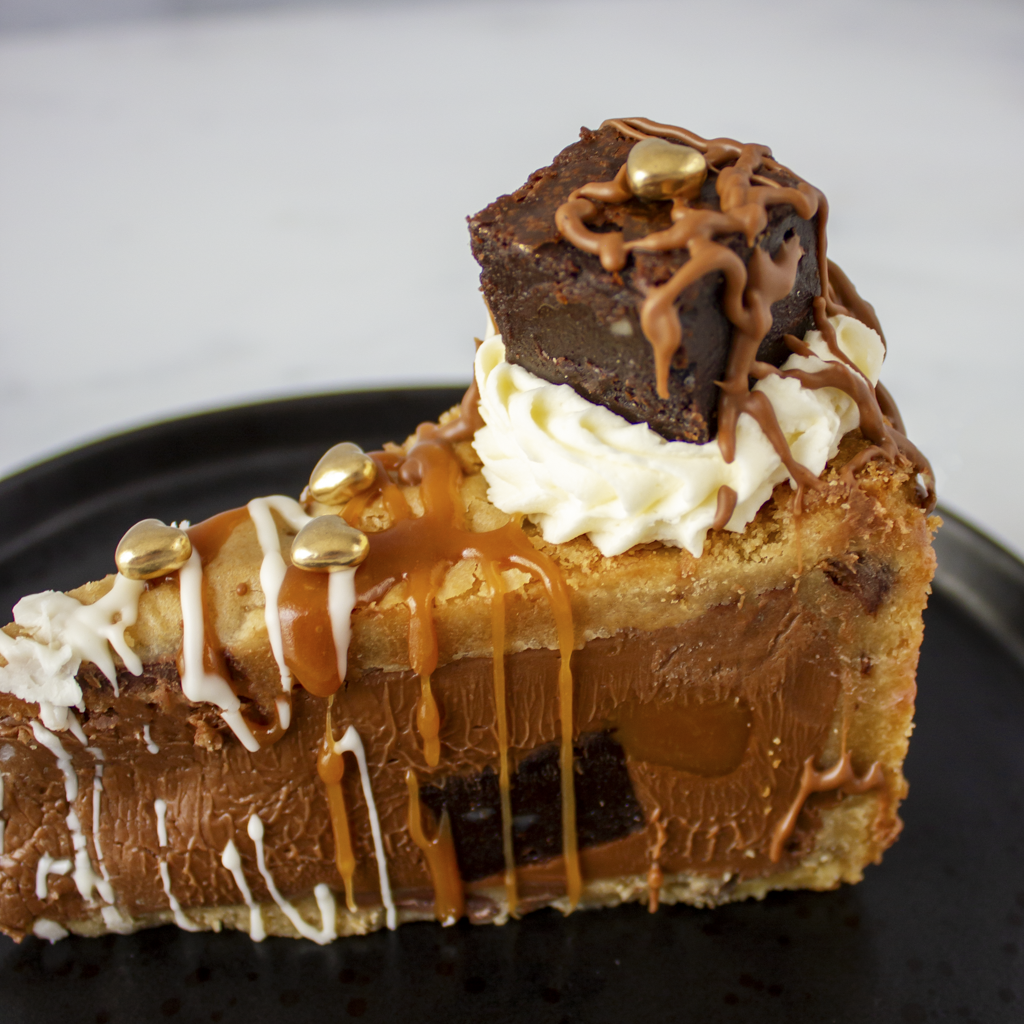 Chocolate dessert with white cream, caramel drizzle, and mini golden chocolate heart decoration on a black plate