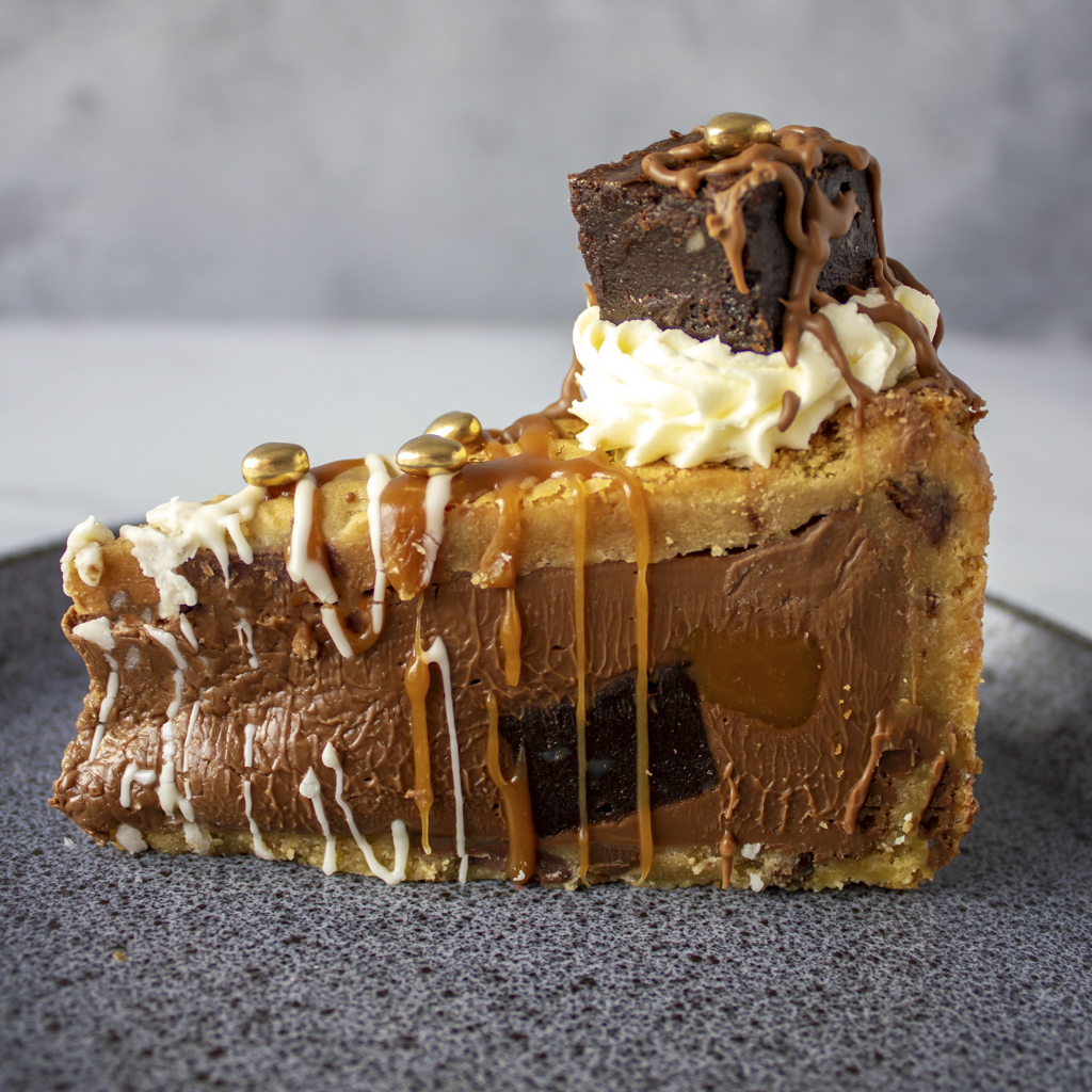 Limited Edition Salted Caramel Brownie Cookie Pie with chocolate, caramel, and white cream on a dark surface.