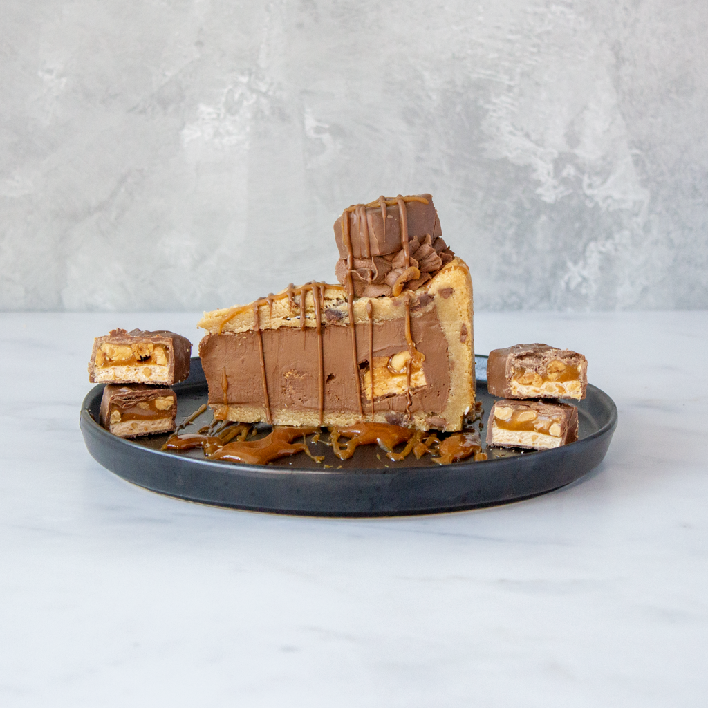 DoughGirl Snickers Cookie Pie Slice served on black plate with chocolate and caramel topping