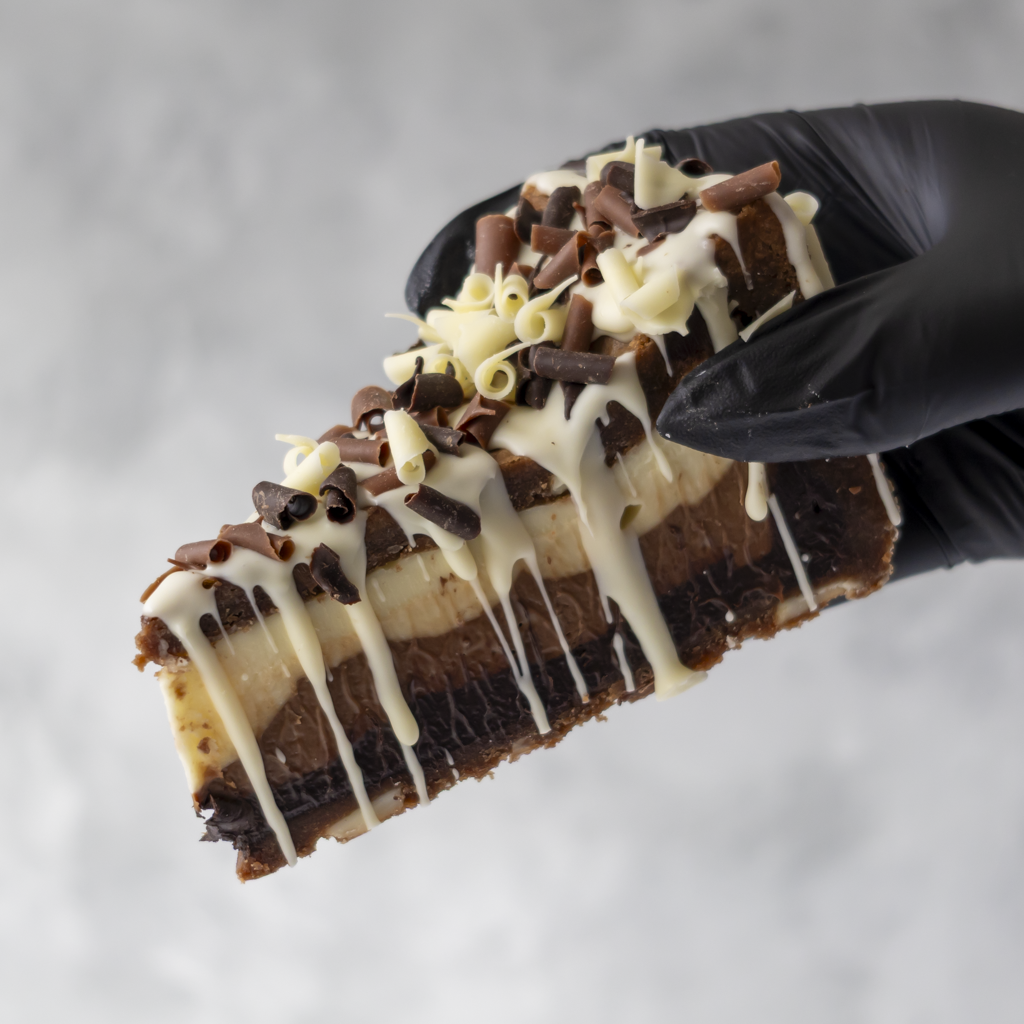 Triple Chocolate Cookie Pie Slice held in black glove with chocolate curls and drizzle