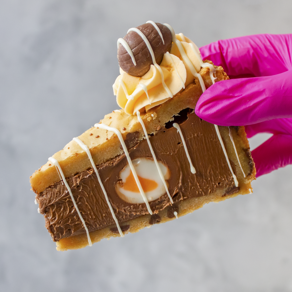 DoughGirl Creme Egg Cookie Pie with a Mini Cream Egg held by a hand wearing a pink glove on a gray background