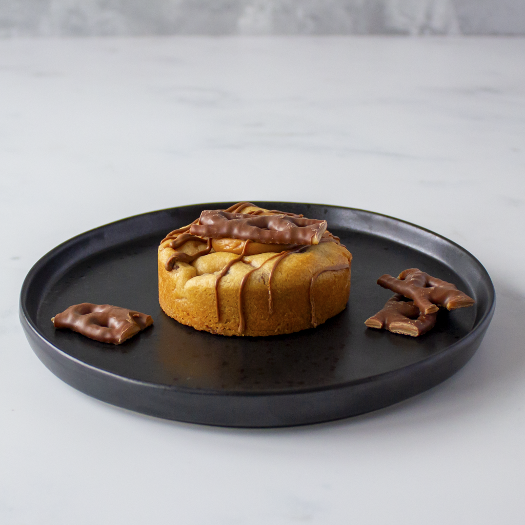 Curly Wurly Stuffed Deluxe Cookie on black plate showing thick golden cookie base