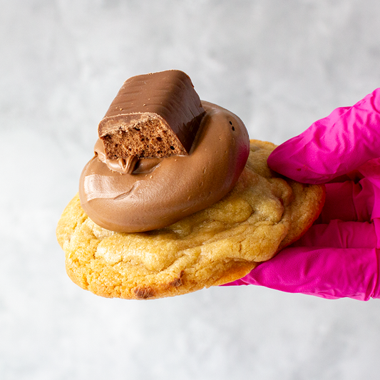 Cadbury Wispa Deluxe Cookie with a chocolate filling held by a pink-gloved hand on a white background