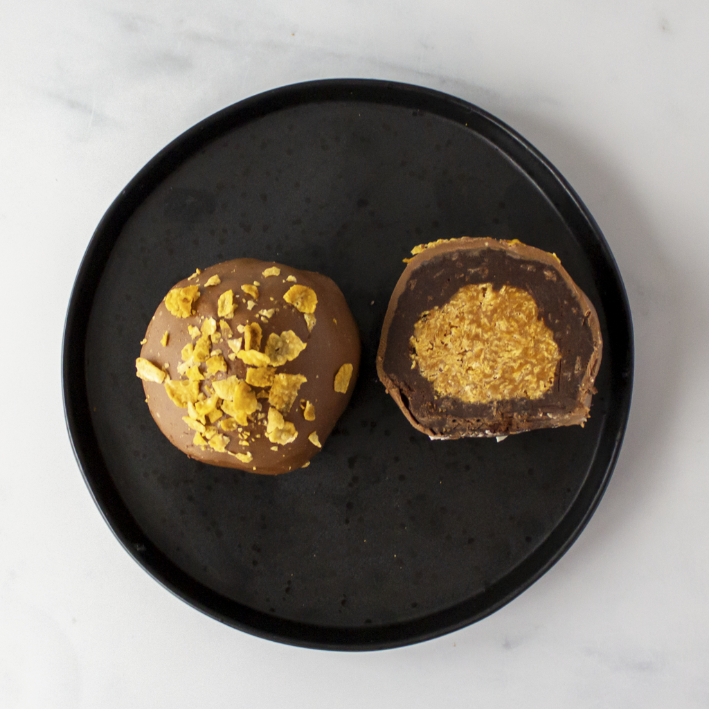 Chocolate truffles with golden caramel cornflake centre on a black plate against a white background