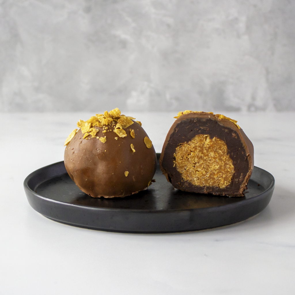 Chocolate Boom Bites with a golden caramel cornflake centre on a black plate against a gray background