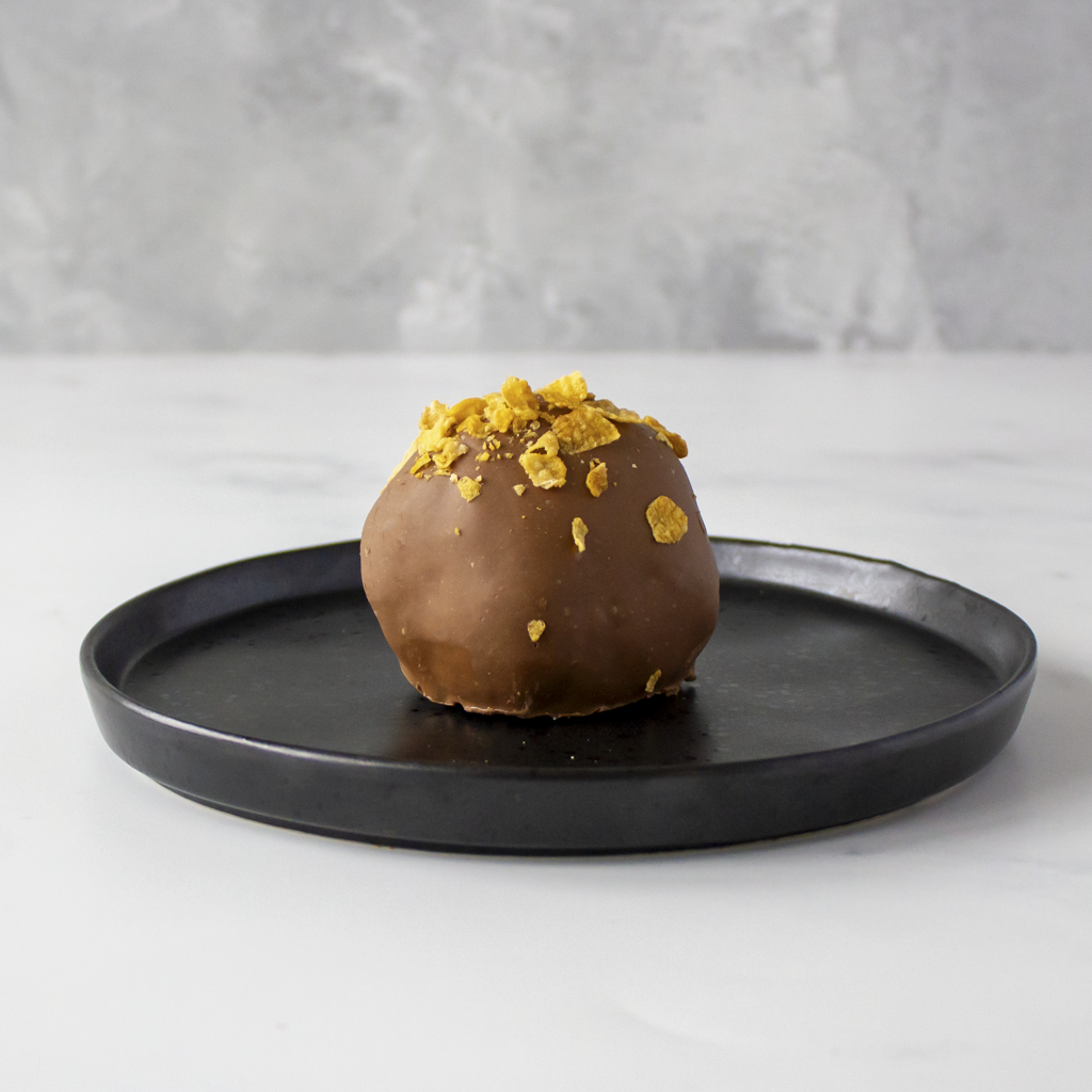 Chocolate dessert with cornflake toppings on a black plate against a gray background