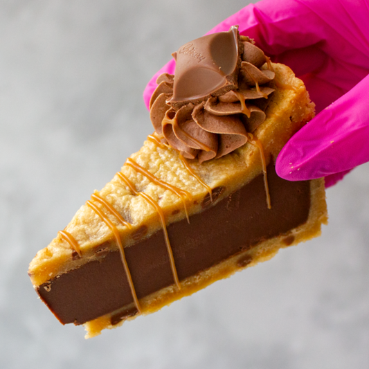 Slice of Caramel Cookie Pie with a drizzle held by a gloved hand against a neutral background