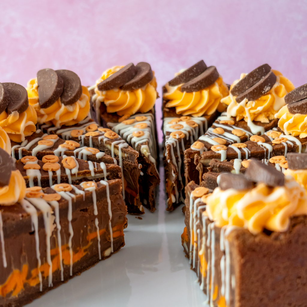 Chocolate & Orange Fright Cookie Pie topped with orange frosting, white drizzle, and chocolate pieces, arranged on a white plate against a soft pink background.