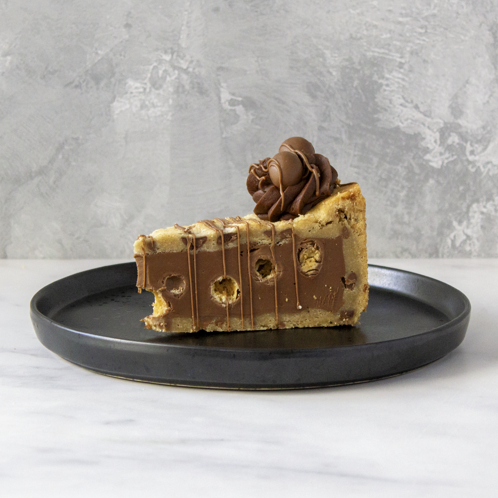 Slice of chocolate cake with chocolate drizzle and frosting on a black plate against a gray background