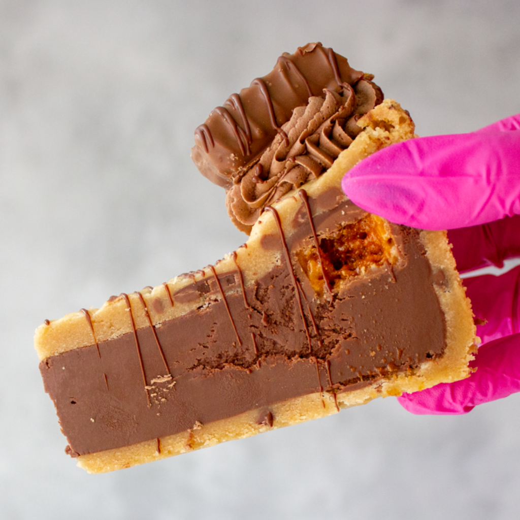 DoughGirl Crunchie Cookie Pie Slice with a pink gloved hand holding it against a neutral background