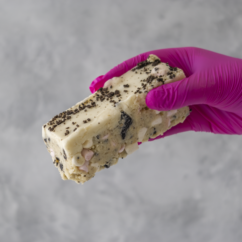 Cookies and Cream Rocky Mountain Road cake held by hand with pink glove on grey background