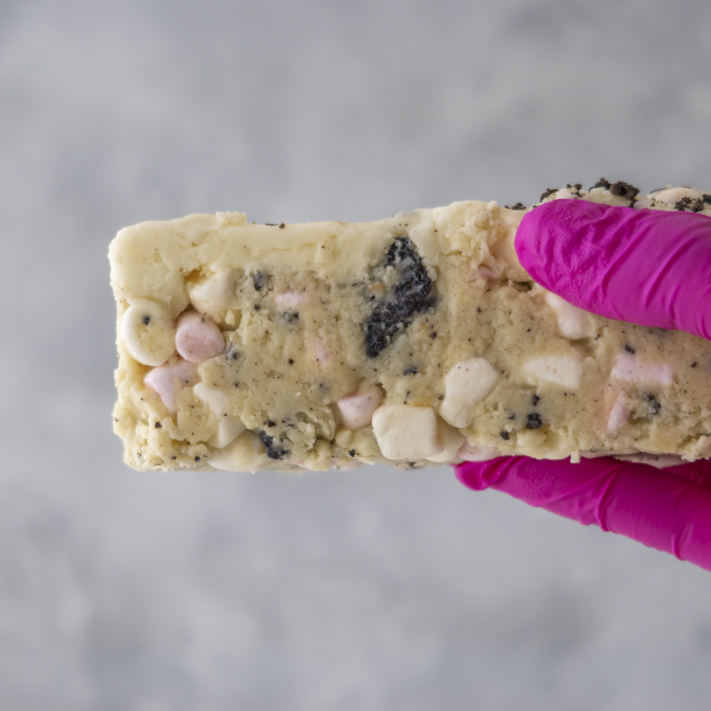 Hand holding Cookies and Cream Rocky Mountain Road cake with pink glove on a grey background