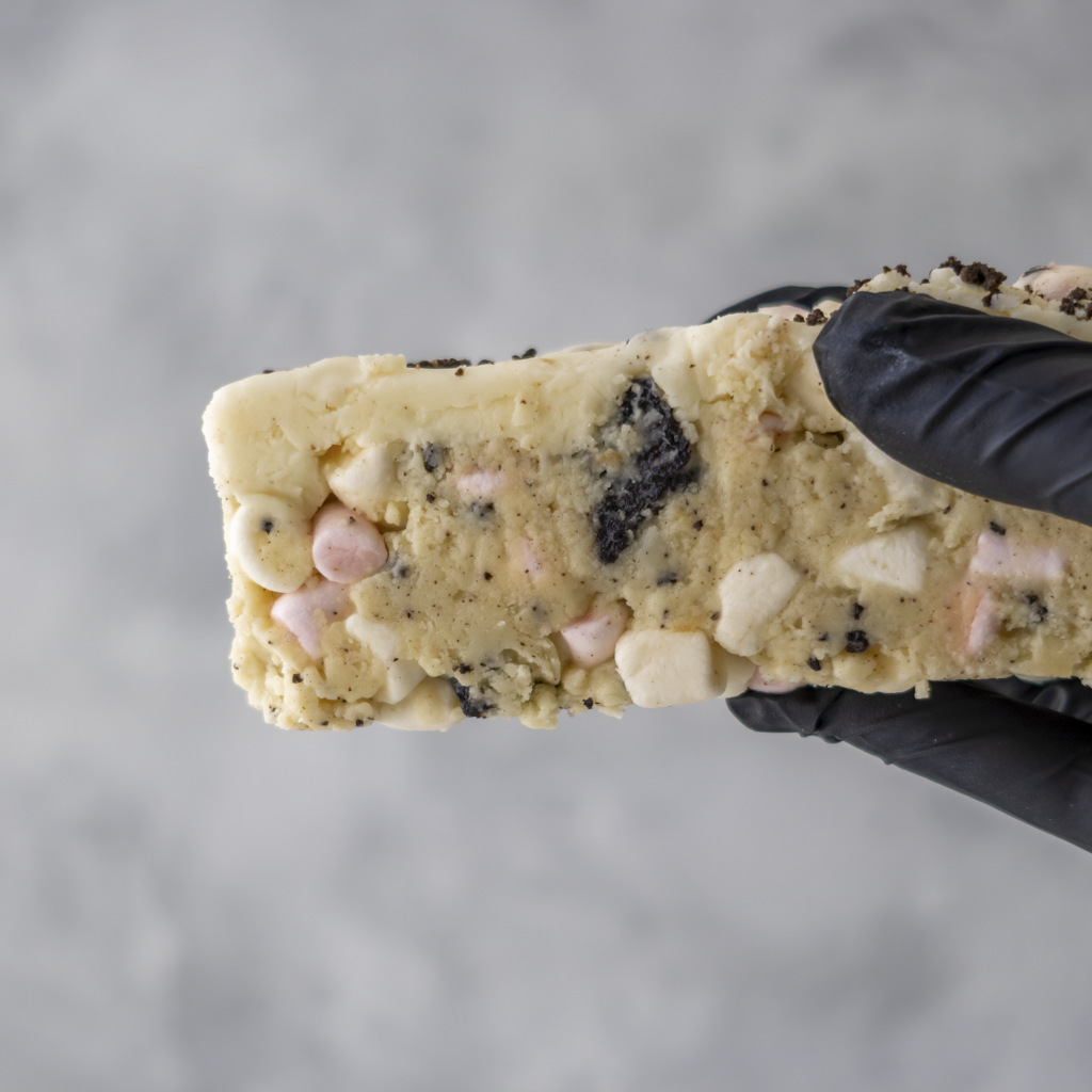 Cookies and Cream Rocky Mountain Road cake held by hand with black glove on grey background