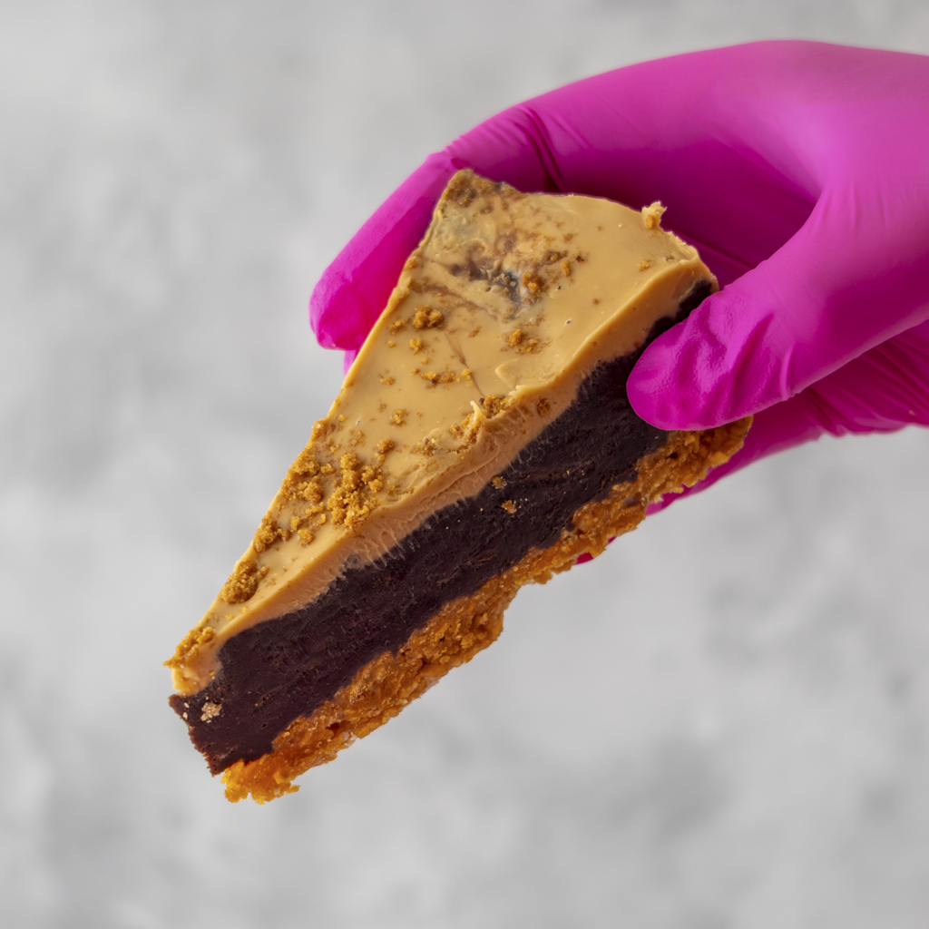 Cornflake Brownie Biscoff Pie Slice held by a hand wearing a pink glove on a neutral background