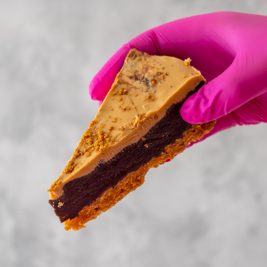 Cornflake Brownie Biscoff Pie Slice held by a hand wearing a pink glove on a neutral background
