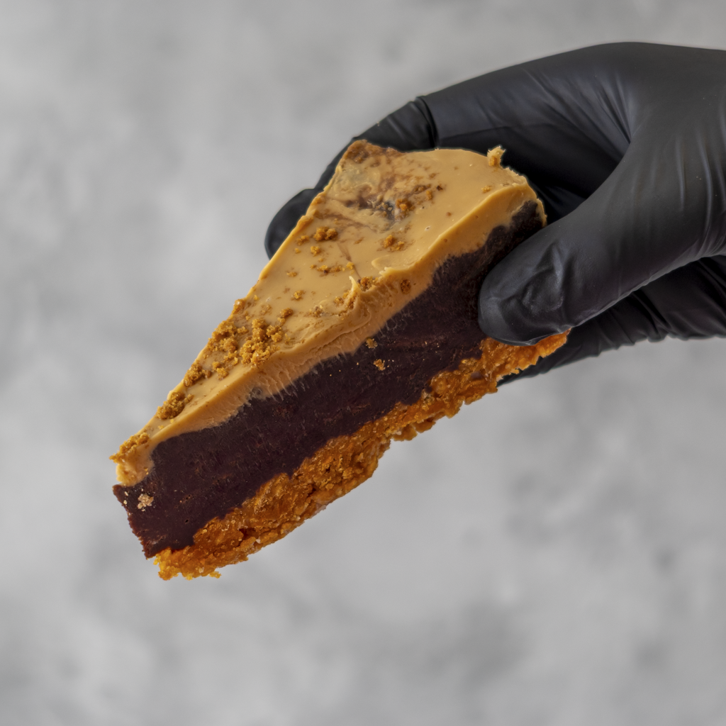 Slice of layered dessert held by a black gloved hand against a neutral background