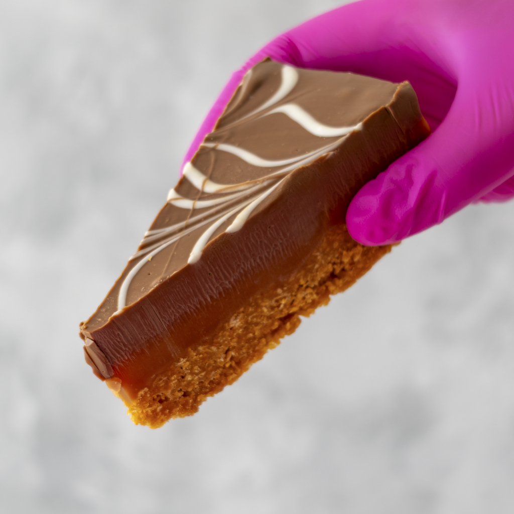DoughGirl Millionaire Cornflake Pie Slice held in pink glove with chocolate topping