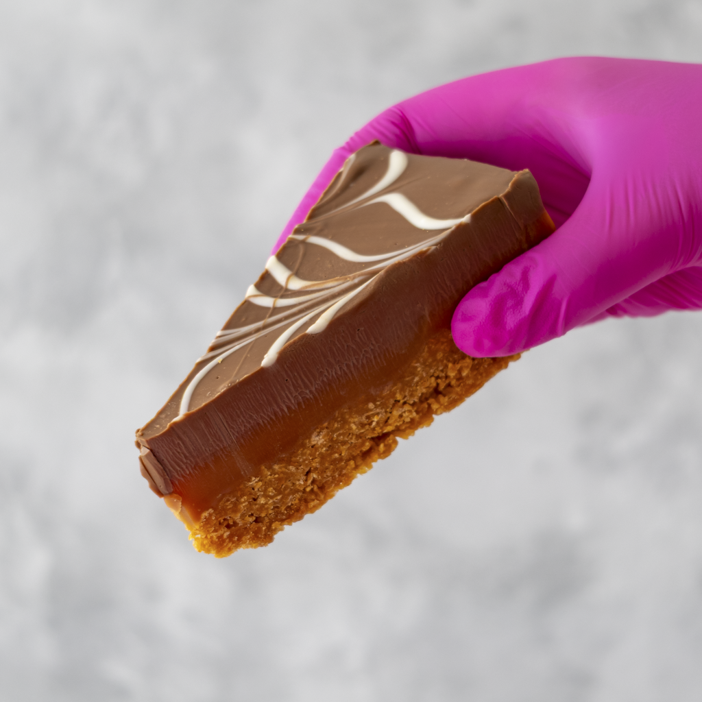 DoughGirl Millionaire Cornflake Pie Slice held in pink glove on grey background