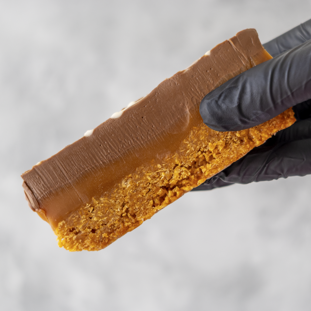 Millionaire Cornflake Pie Slice held in black glove showing caramel cornflake base