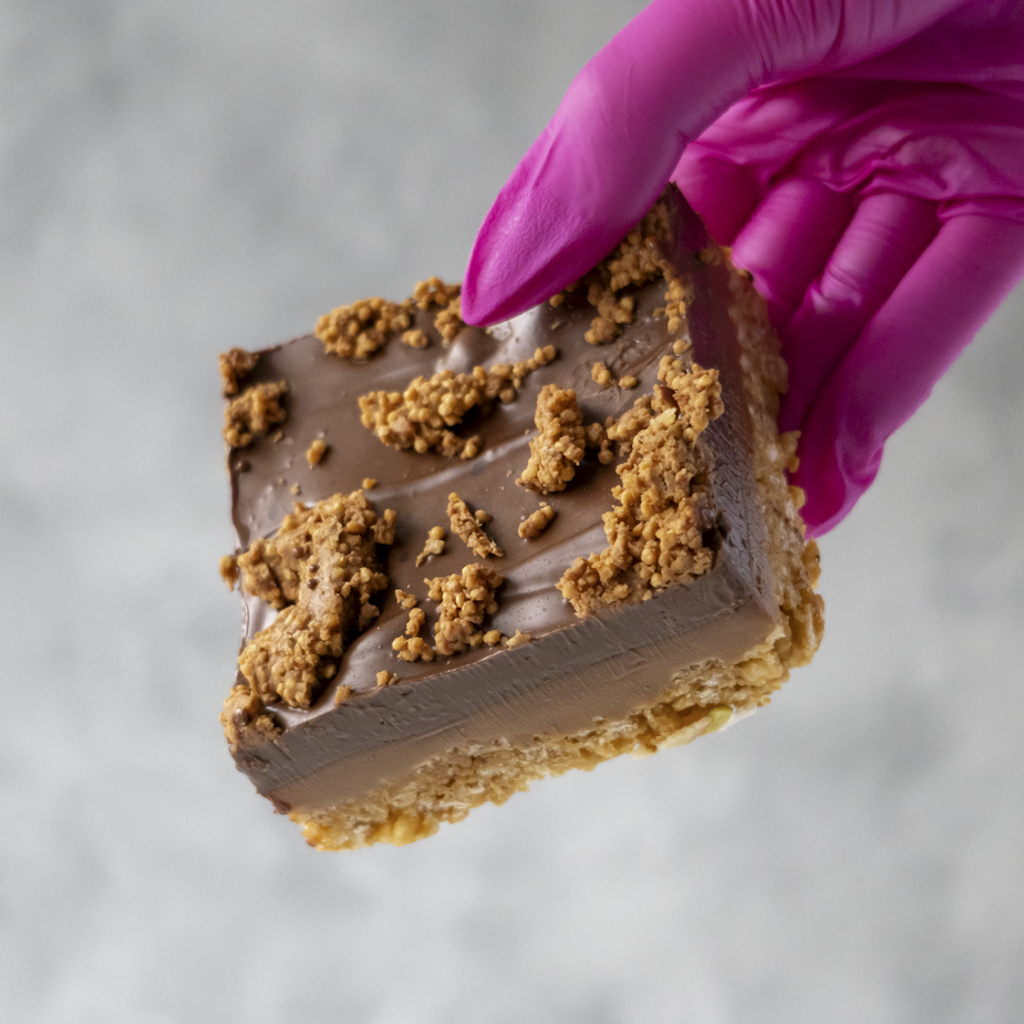 Cracking Caramel Crispie Slab held by a hand in a pink glove on a neutral background