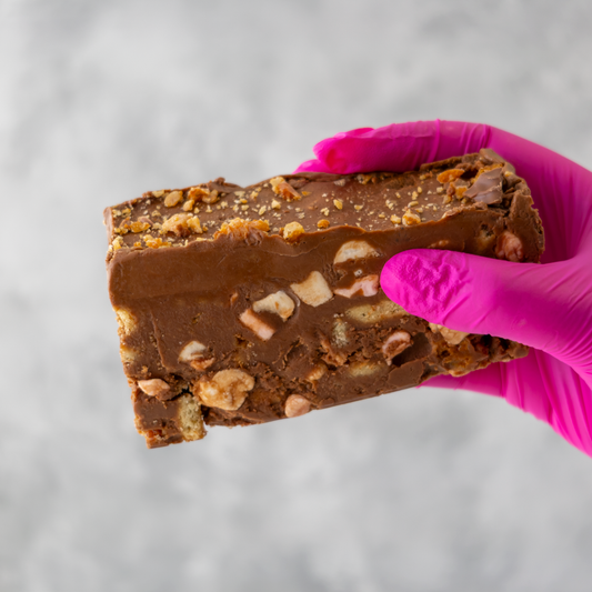 Crunchie Rocky Mountain Road cake held by hand with pink glove on light gray background