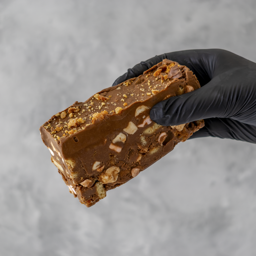 Hand holding a Crunchie Rocky Mountain Road cake with a black glove against a gray background