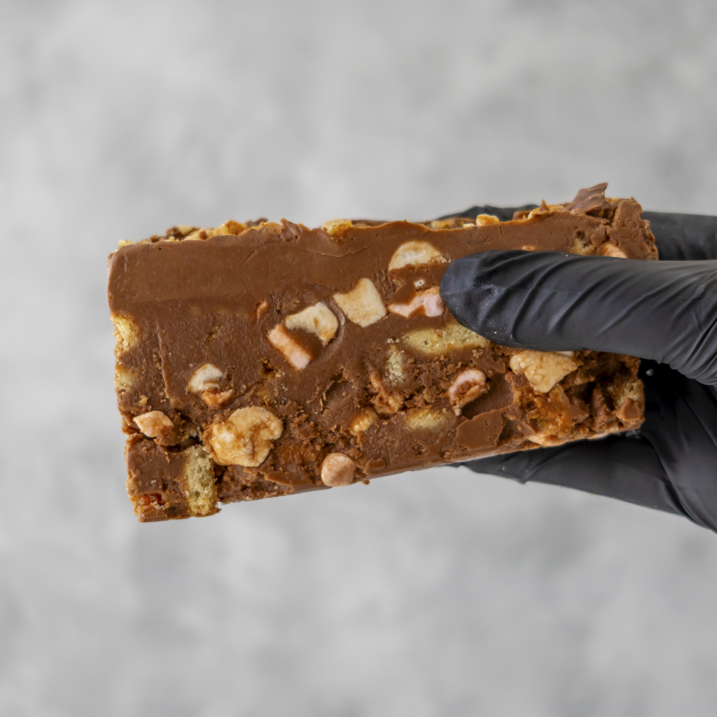 Crunchie Rocky Mountain Road cake with nuts held by a gloved hand against a gray background