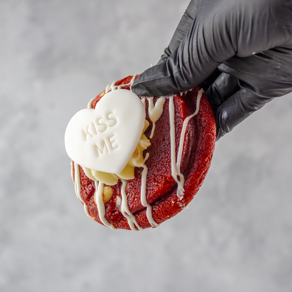Red velvet deluxe cookie by DoughGirl with white icing and 'Kiss Me' heart on a gray background