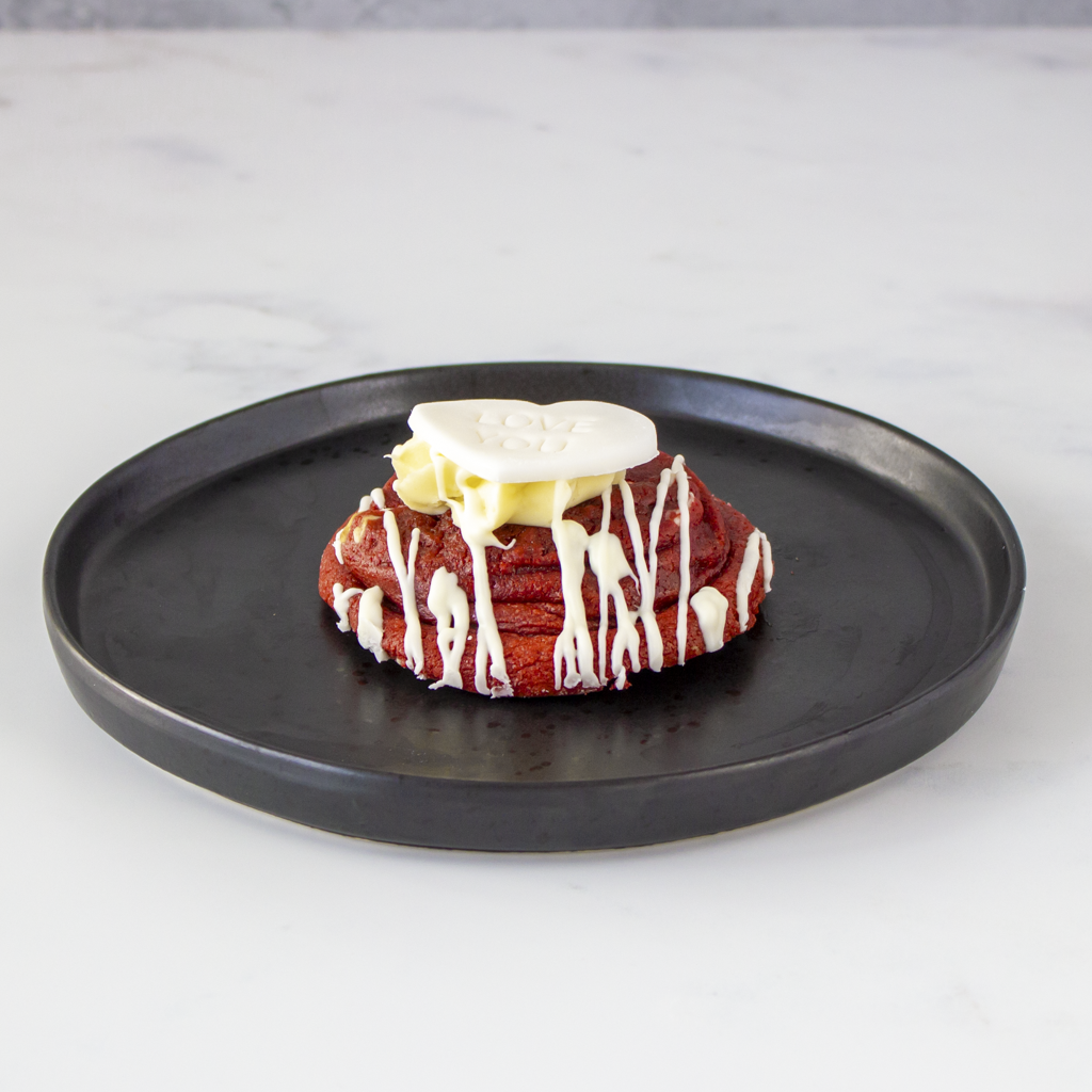 Red velvet deluxe cookie with white frosting on a black plate