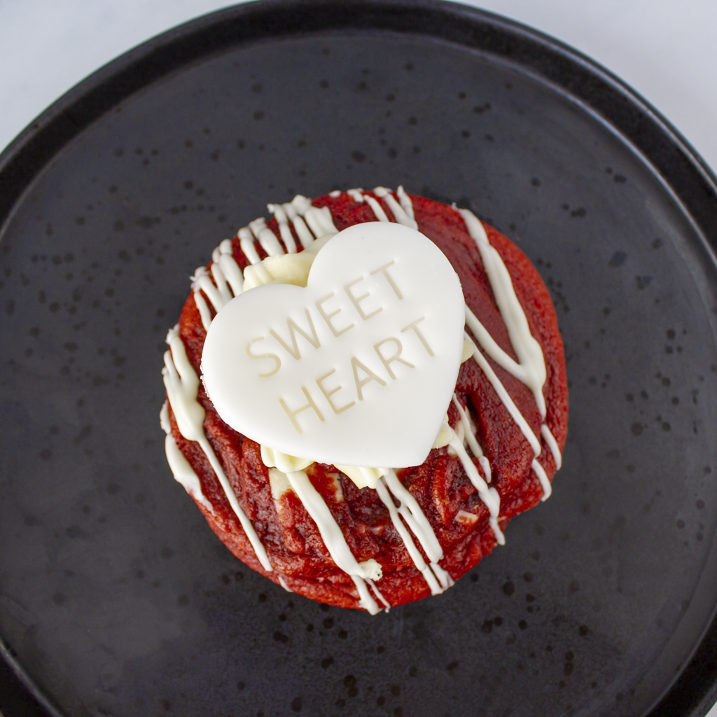 Red velvet cupcake with white drizzle and 'sweet heart' candy on a black plate