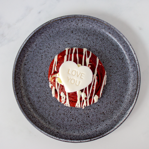 Red velvet cookie with white chocolate drizzle and 'LOVE YOU' message on a gray plate.