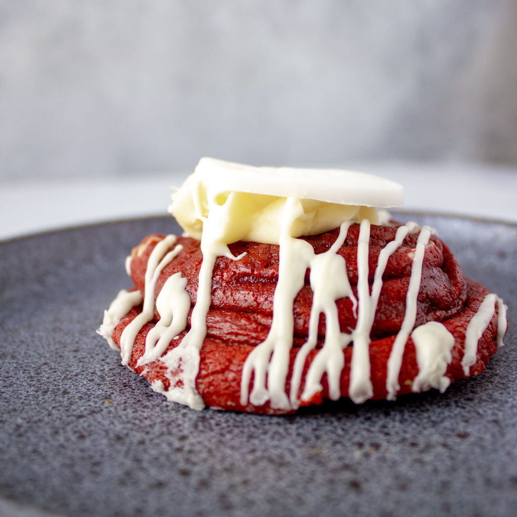 Red velvet cookie with cream cheese and white chocolate frosting on a dark plate