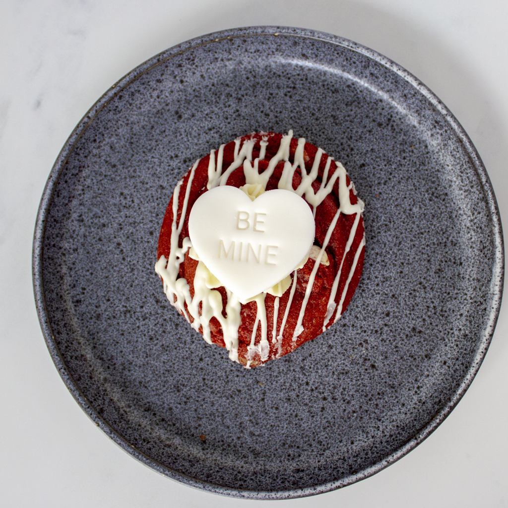 Red velvet cookie dessert with white chocolate heart "BE MINE" on a gray plate