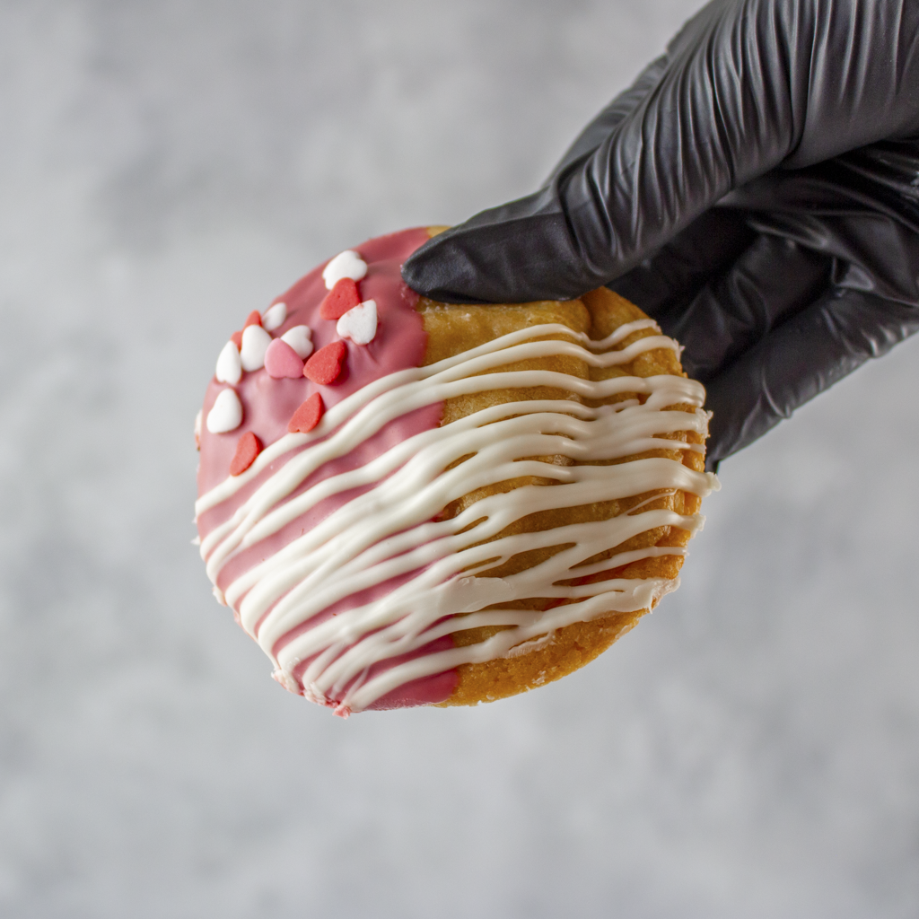 Valentine's Ruby Chocolate Deluxe Cookie with pink and white icing, heart decorations for Valentine gifting, held by a gloved hand against a gray background