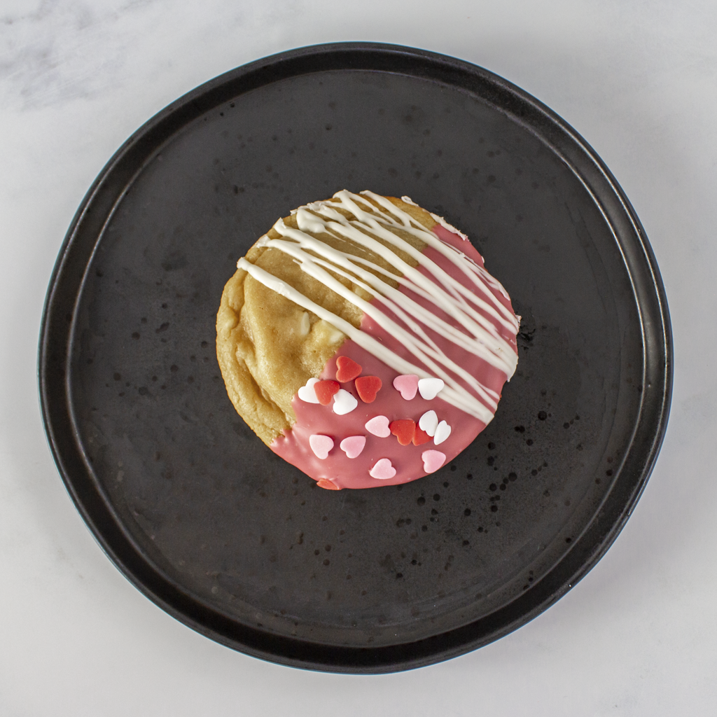 Valentine decorative cookie with white, and pink icing on a black plate.