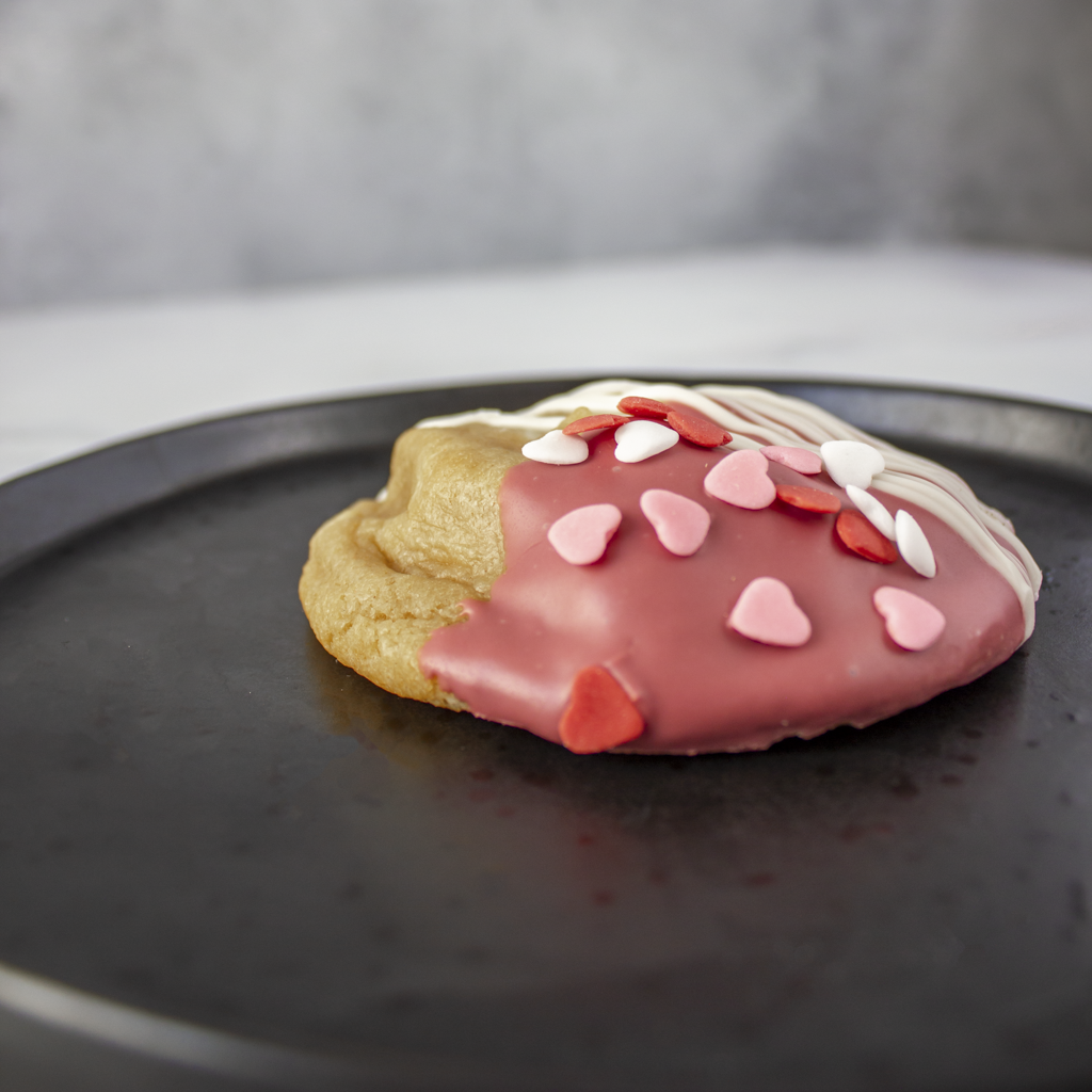 Decorative cookie with pink icing and Valentine heart sprinkles on a black plate.