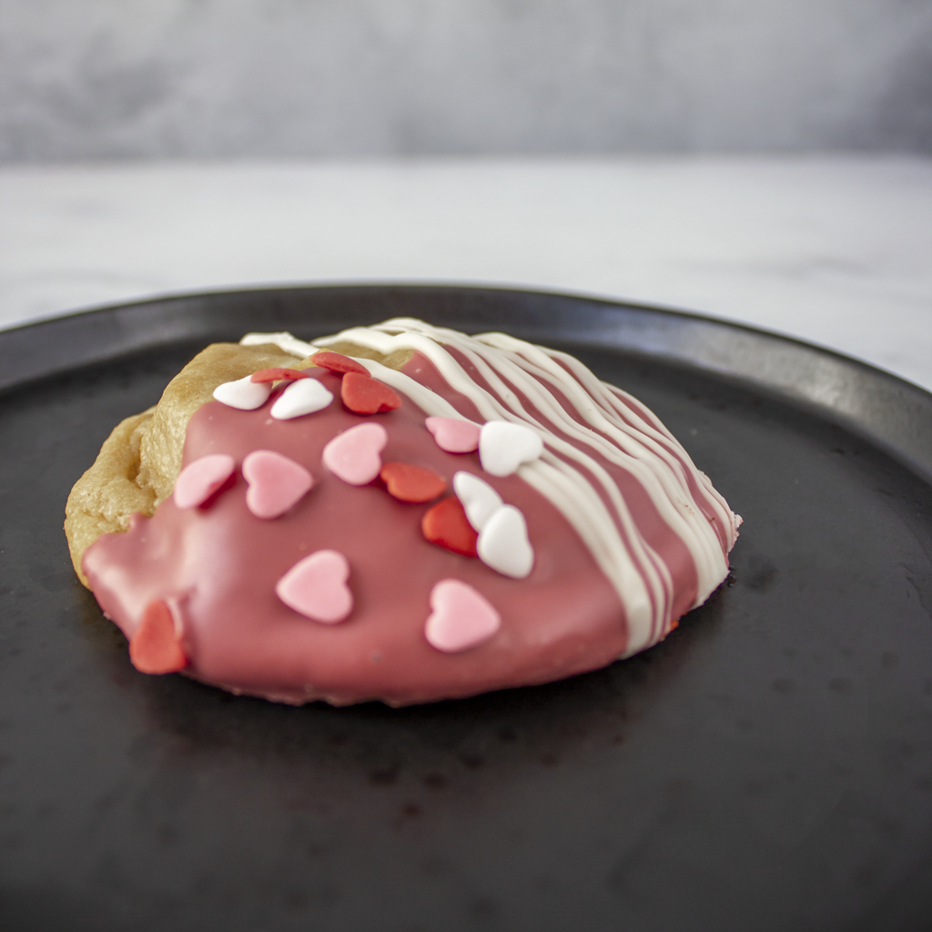 Valentine's Ruby Chocolate Deluxe Cookie with pink and white icing on a black plate