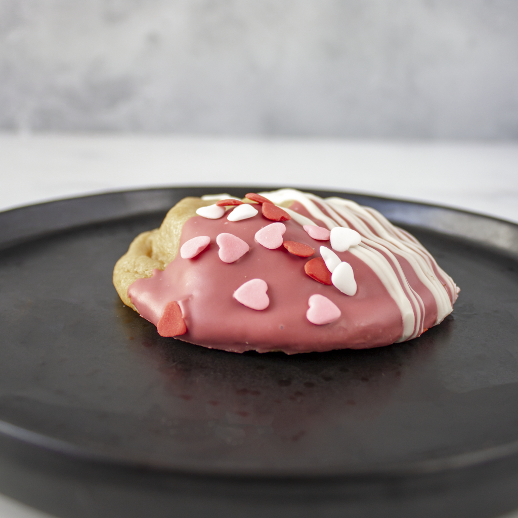 Valentine pastry with pink icing and heart decorations on a black plate