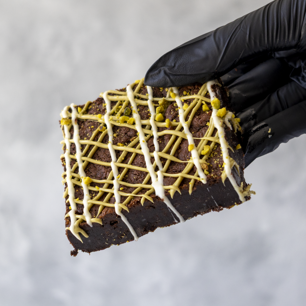 DoughGirl Pistachio Brownie Slab held in black glove showing fudgy brownie base
