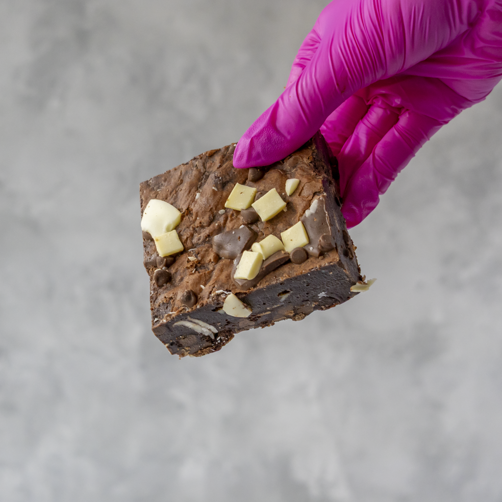 DoughGirl Triple Chocolate Brownie Slab with three types of premium chocolate chips held by a hand in a pink glove on a gray background