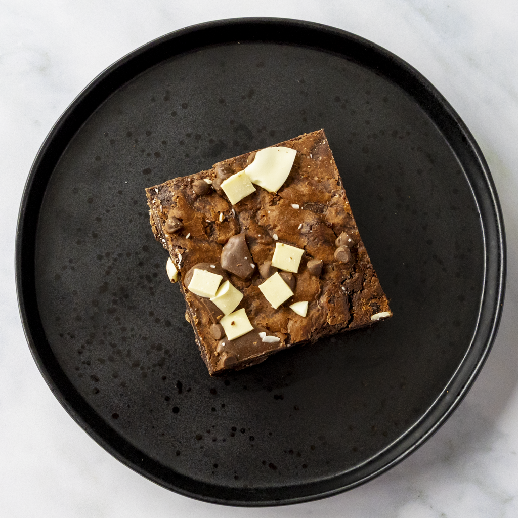 Brownie with white chocolate pieces on a black plate. UK-wide delivery and cookie online delivery available