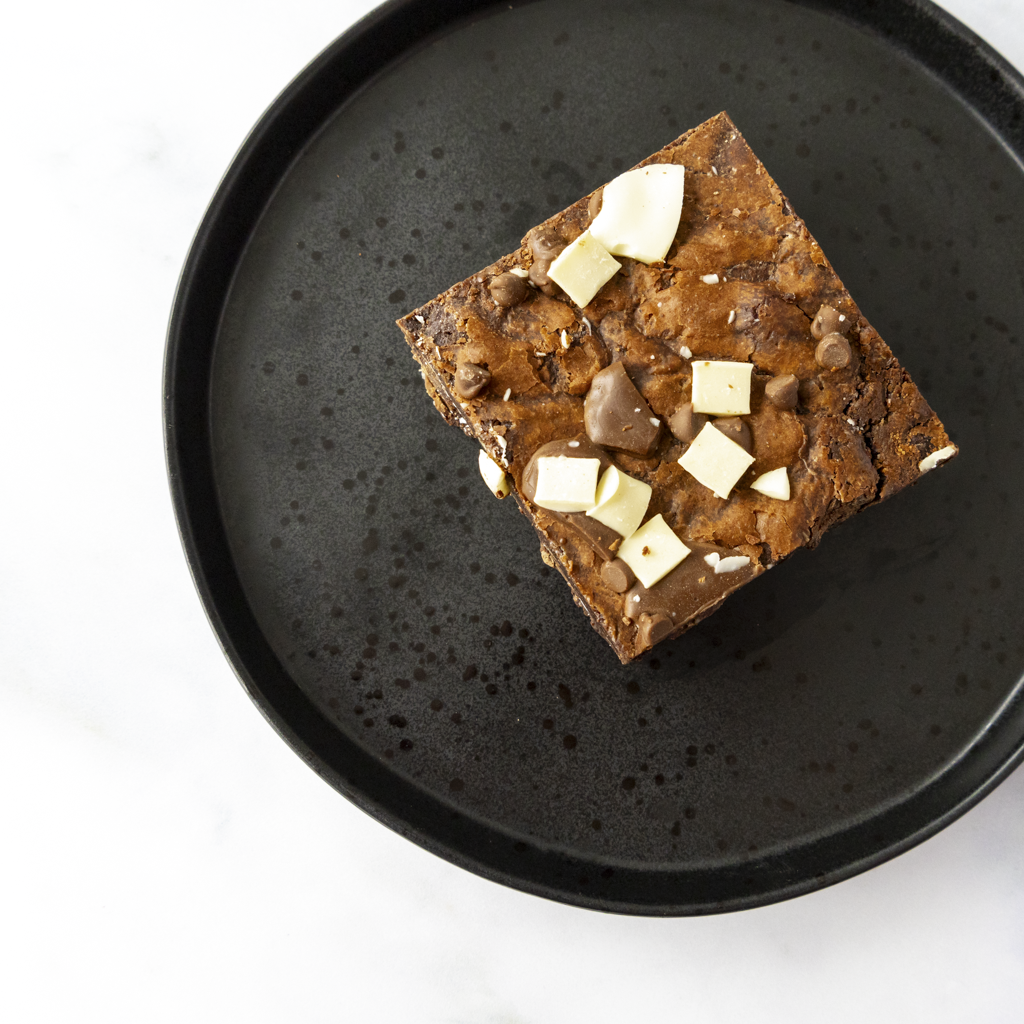 Square of chocolate brownie with with a perfectly baked crust on a black plate and ready to eat
